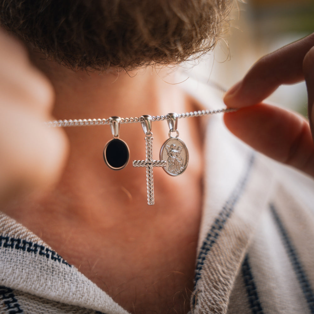 Close-up of a silver necklace with charms held by a person wearing a striped garment.