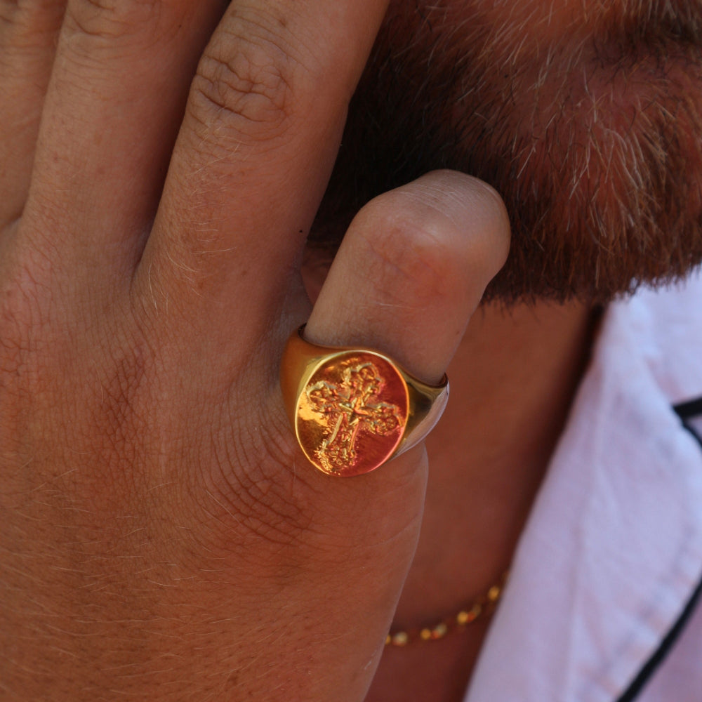 Close-up of a hand wearing a gold ring with a cross design.