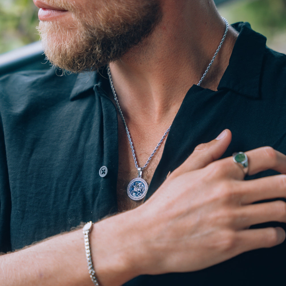 Man wearing a silver necklace, ring, and bracelet with a blurred background
