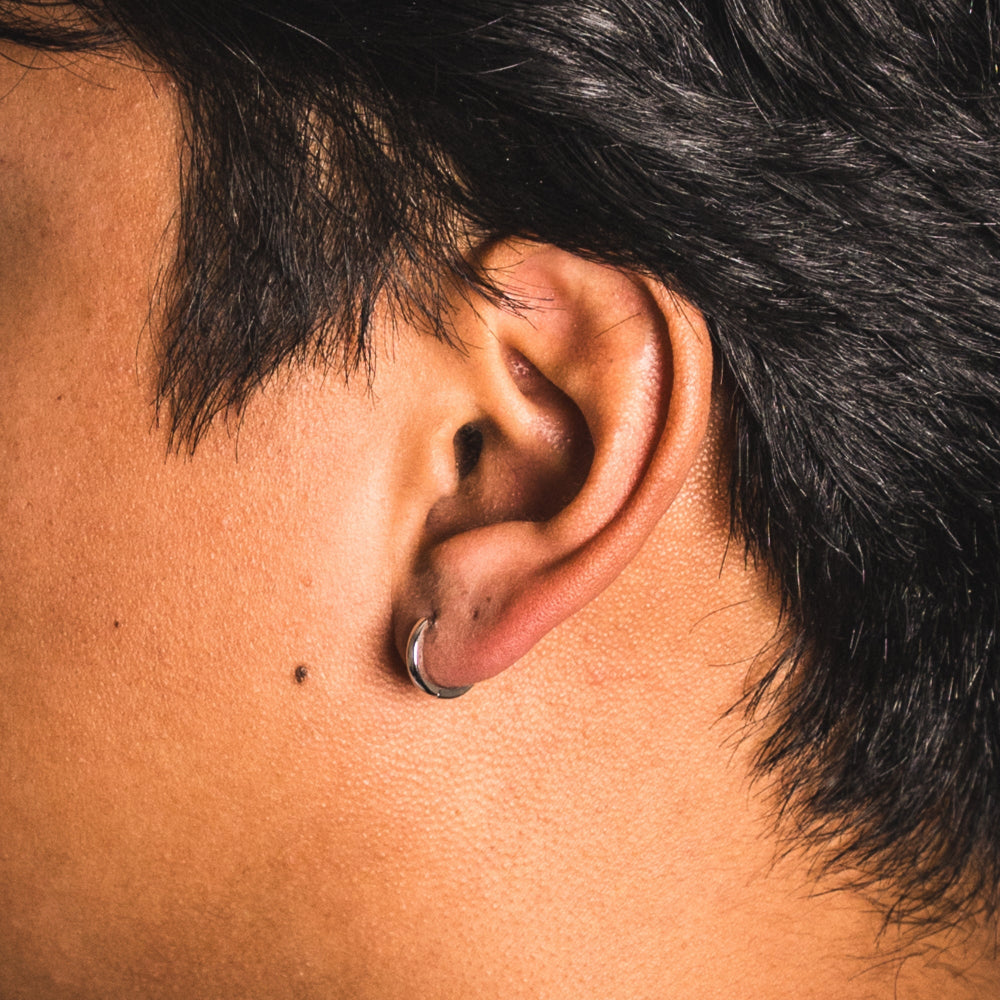 Close-up of an ear with a small earring, surrounded by dark hair.