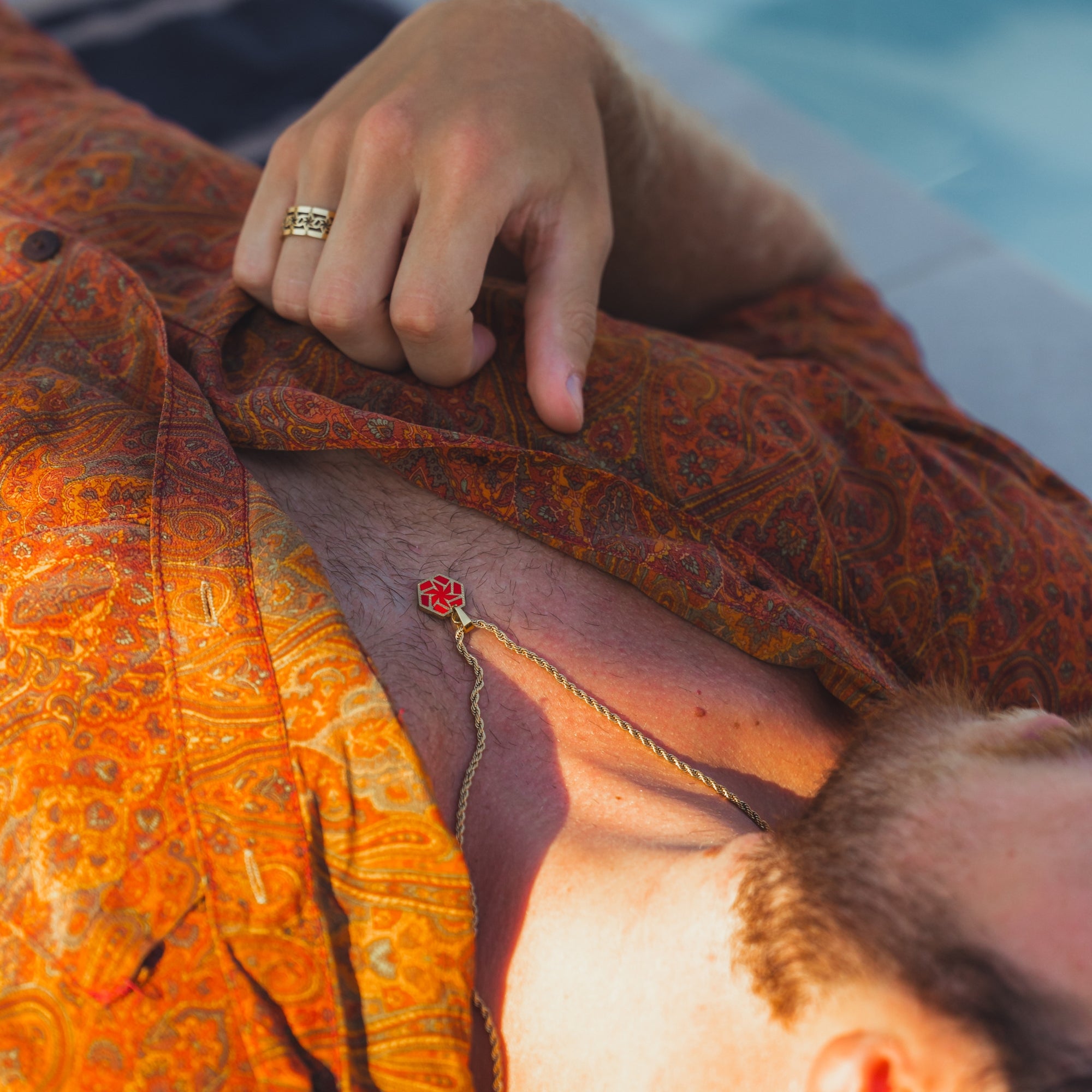 Close-up of a person wearing a patterned shirt with a tattoo on their arm, sitting by a pool.