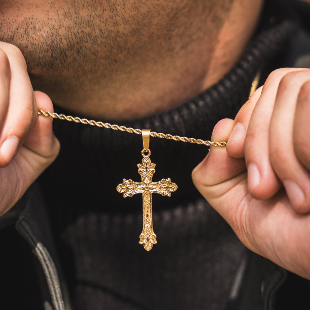 Gold cross necklace held by a person against a dark background