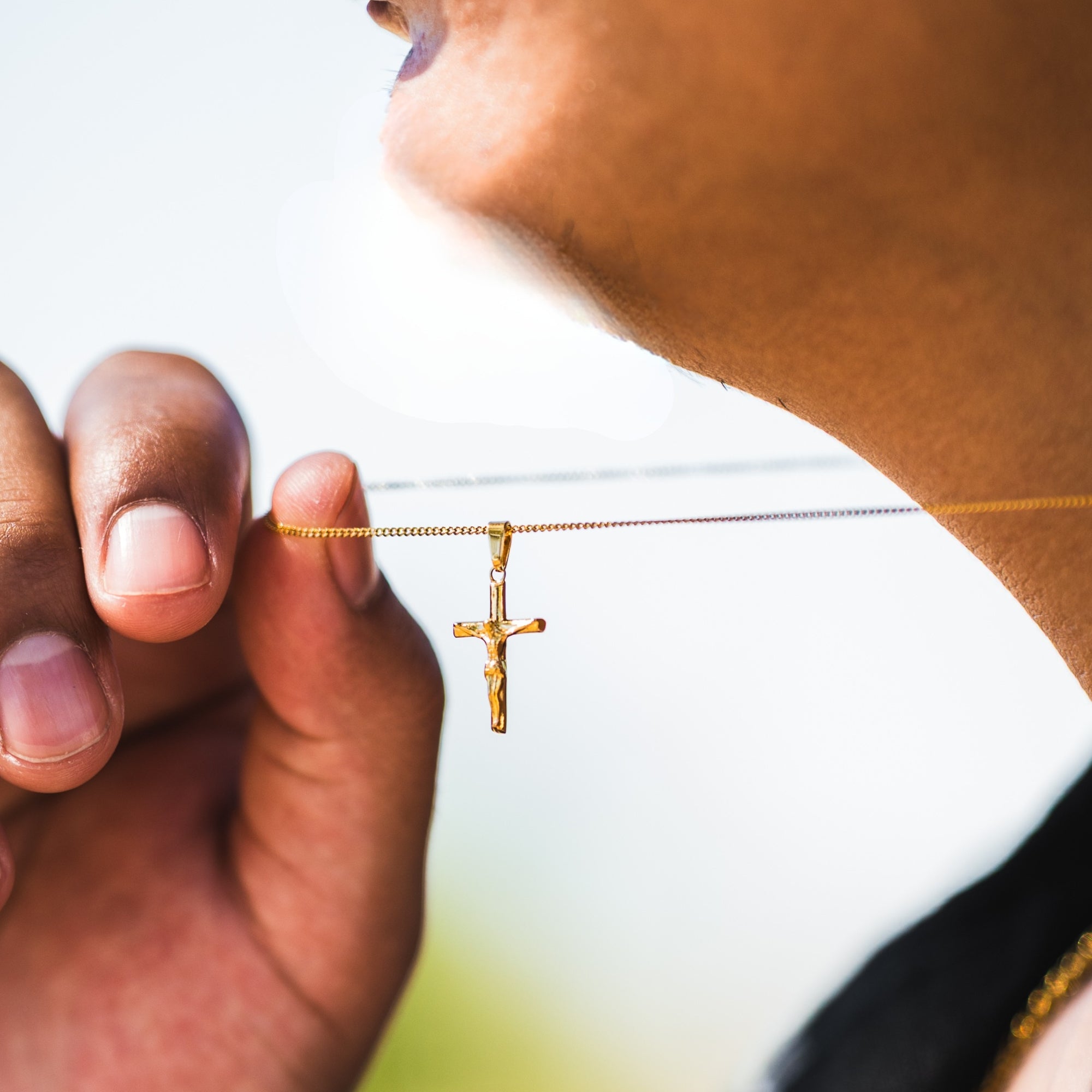 Gold necklace with a cross pendant held by a person against a blurred background