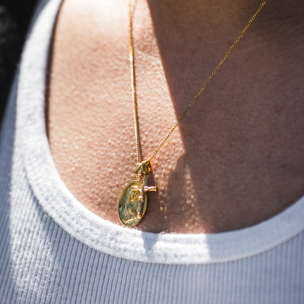 Gold necklace with a pendant on a person wearing a light gray shirt.