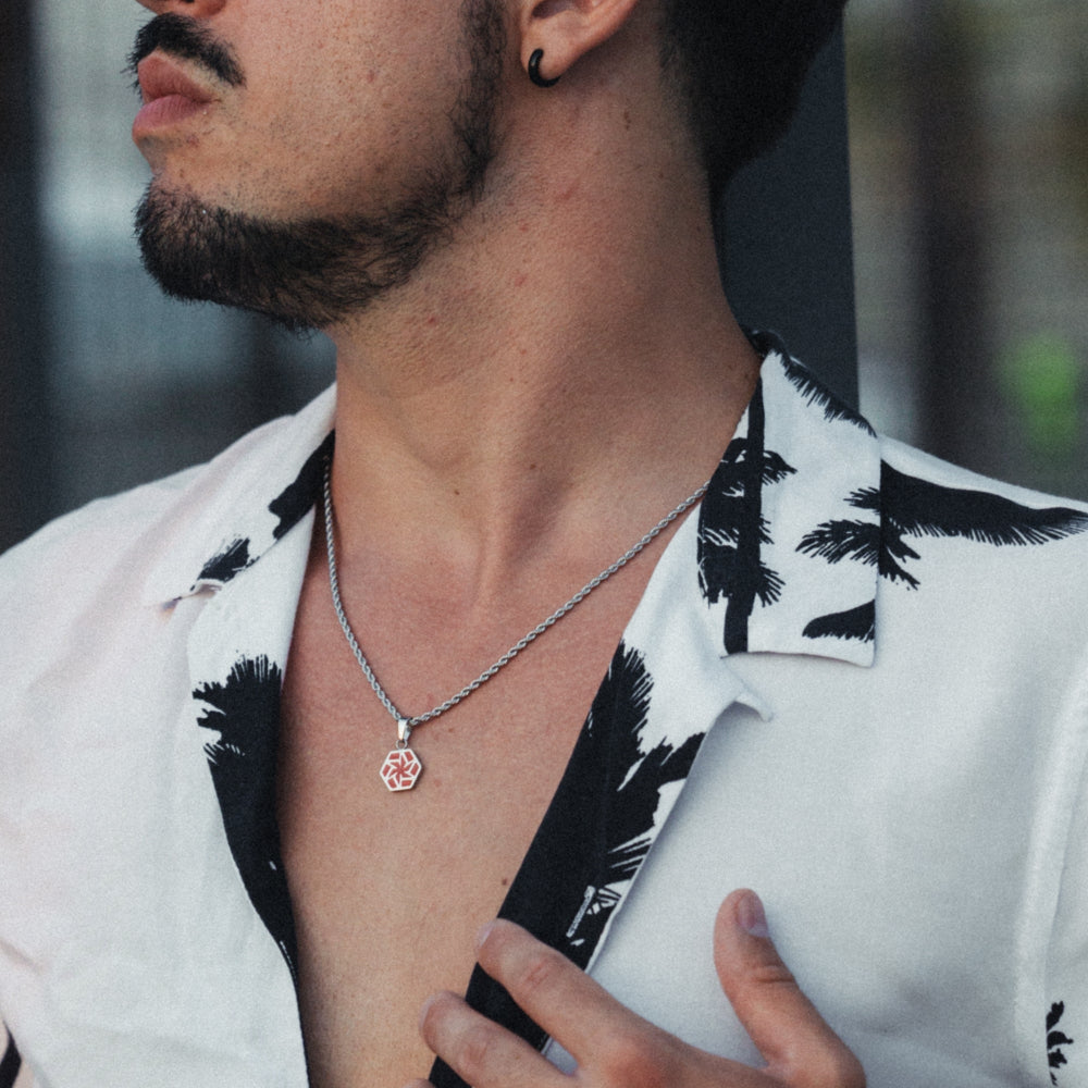 Man wearing a white shirt with black patterns and a necklace with a pendant.