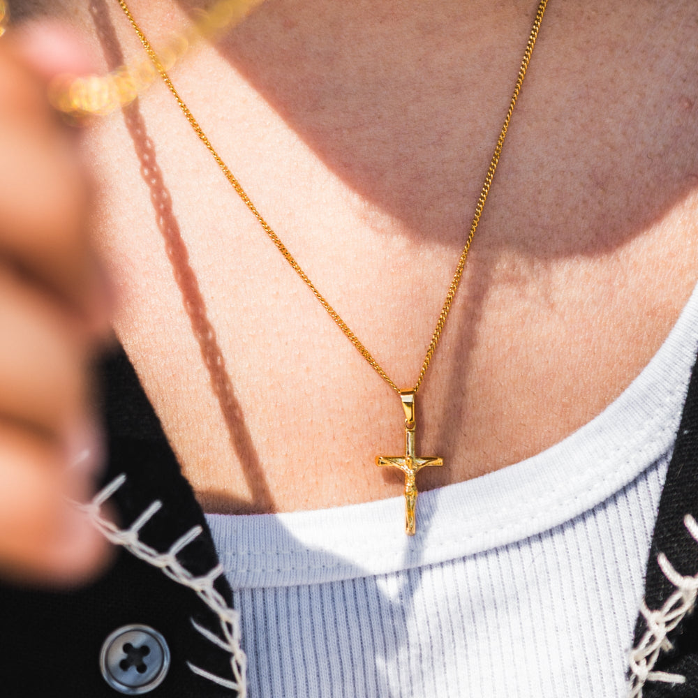 Gold necklace with a cross pendant worn by a person.