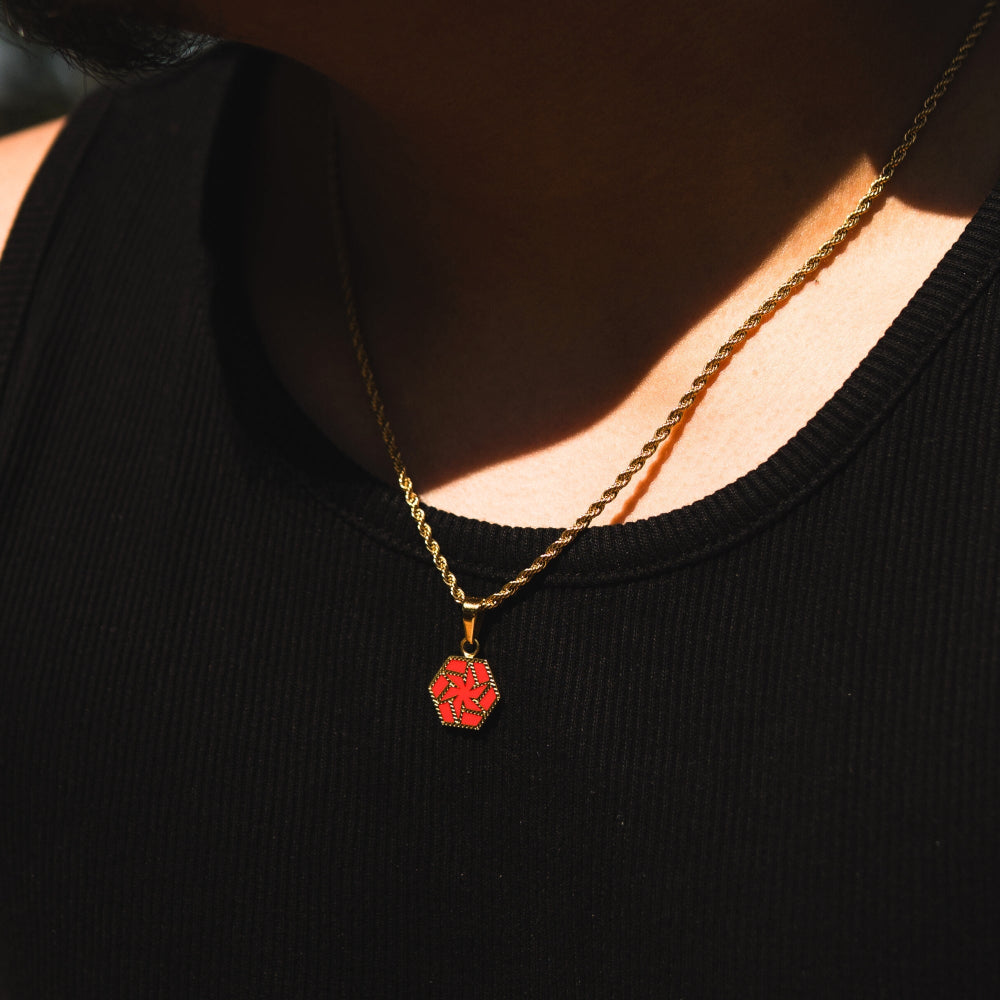 Person wearing a black top with a gold necklace featuring a red hexagonal pendant.