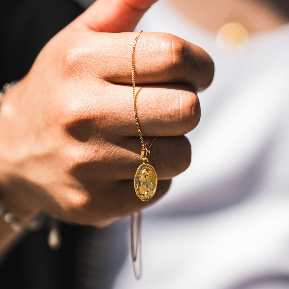 Gold necklace with a pendant held by a hand against a blurred background