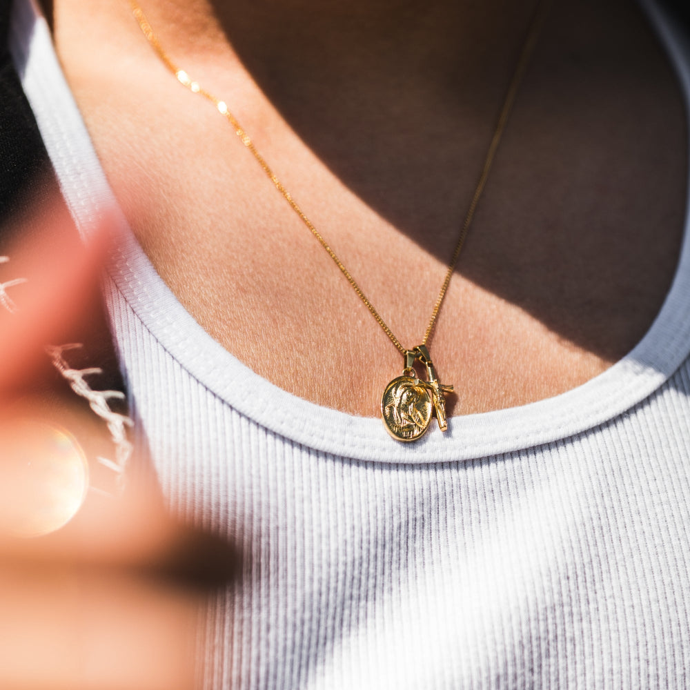 Gold necklace with a pendant on a person wearing a white tank top.