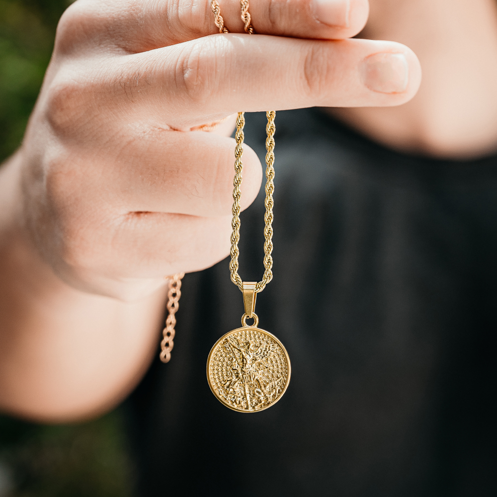 Gold necklace with a round pendant held by a hand against a dark background