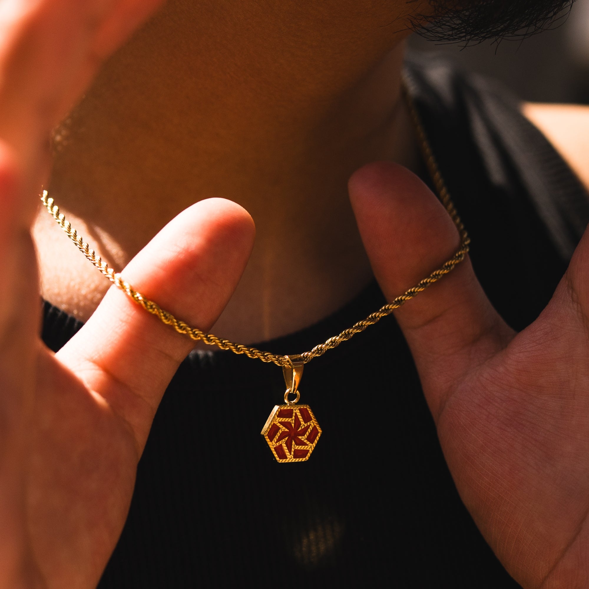 Gold chain necklace with a hexagonal pendant held by hands against a blurred background