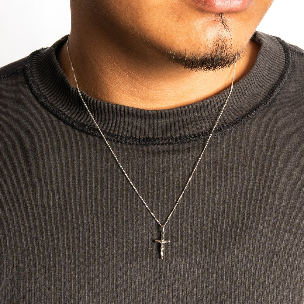 Person wearing a black sweater with a necklace featuring a cross pendant.