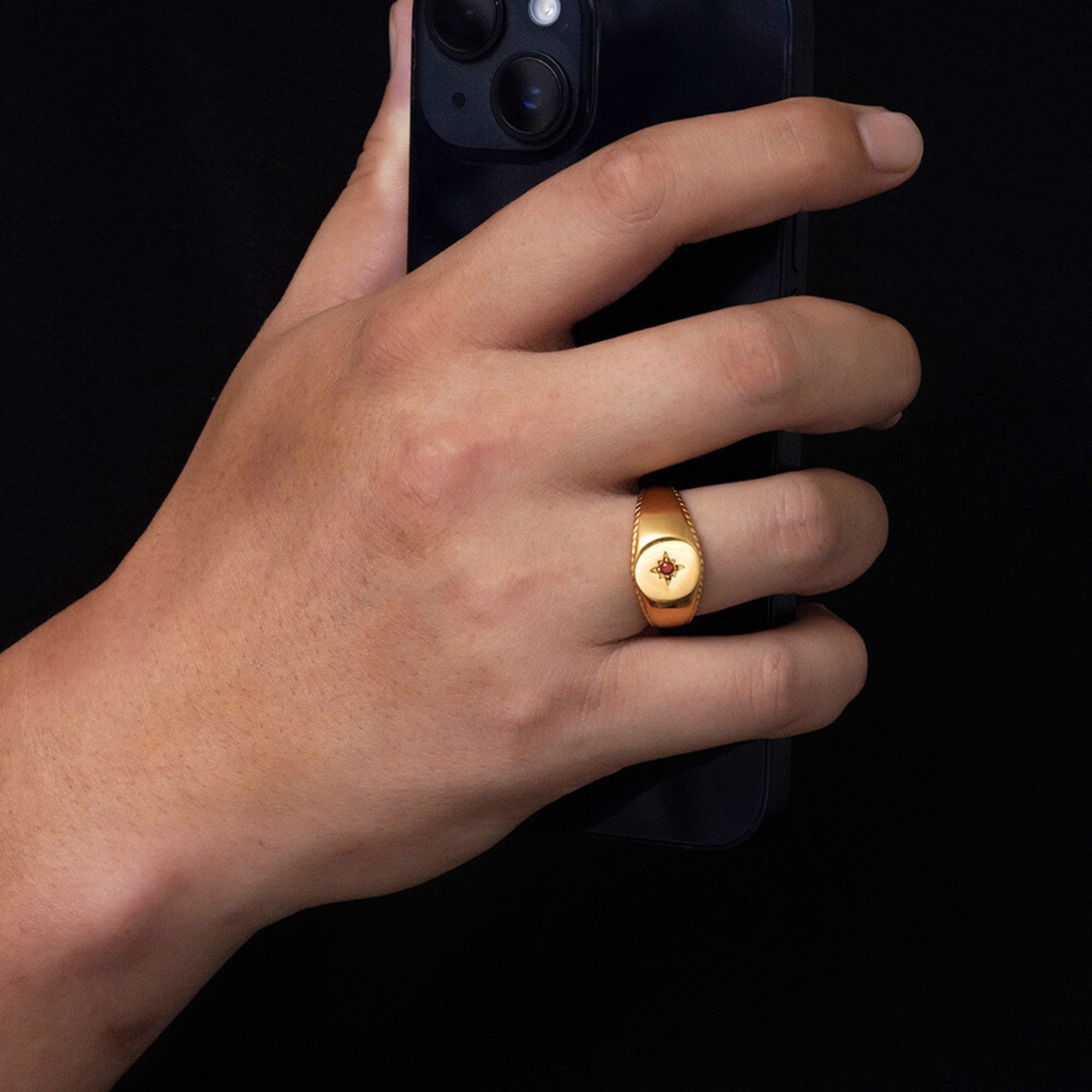 Hand wearing a gold ring holding a smartphone on a black background