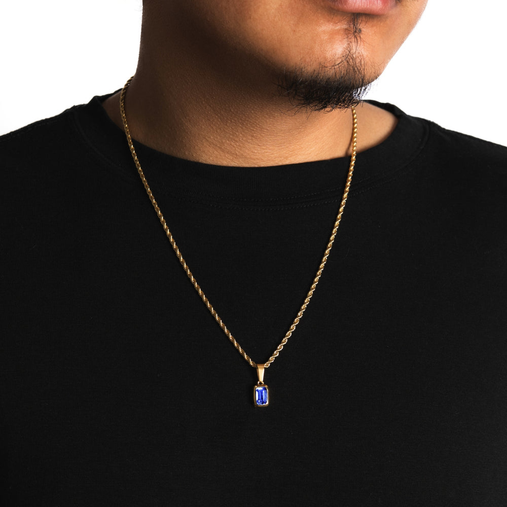 Gold necklace with a blue pendant worn by a person on a black background