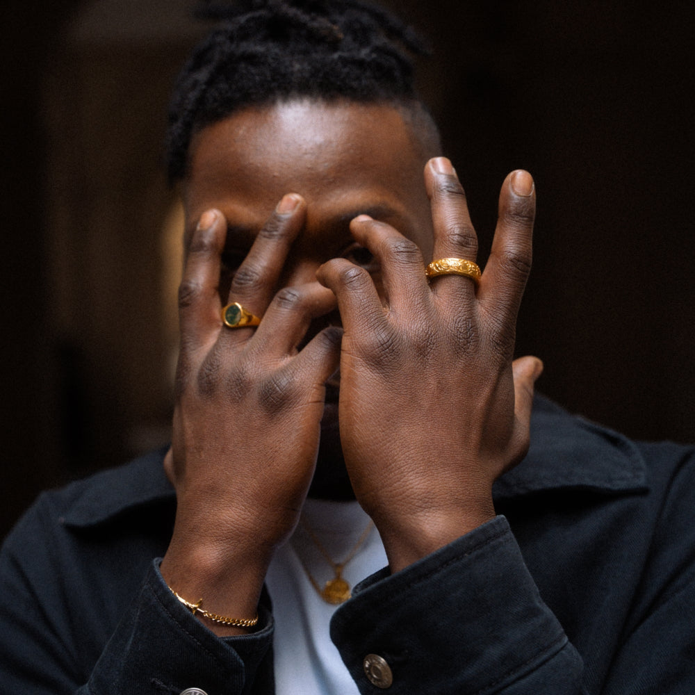 Person covering their face with their hands, wearing gold rings and bracelets.