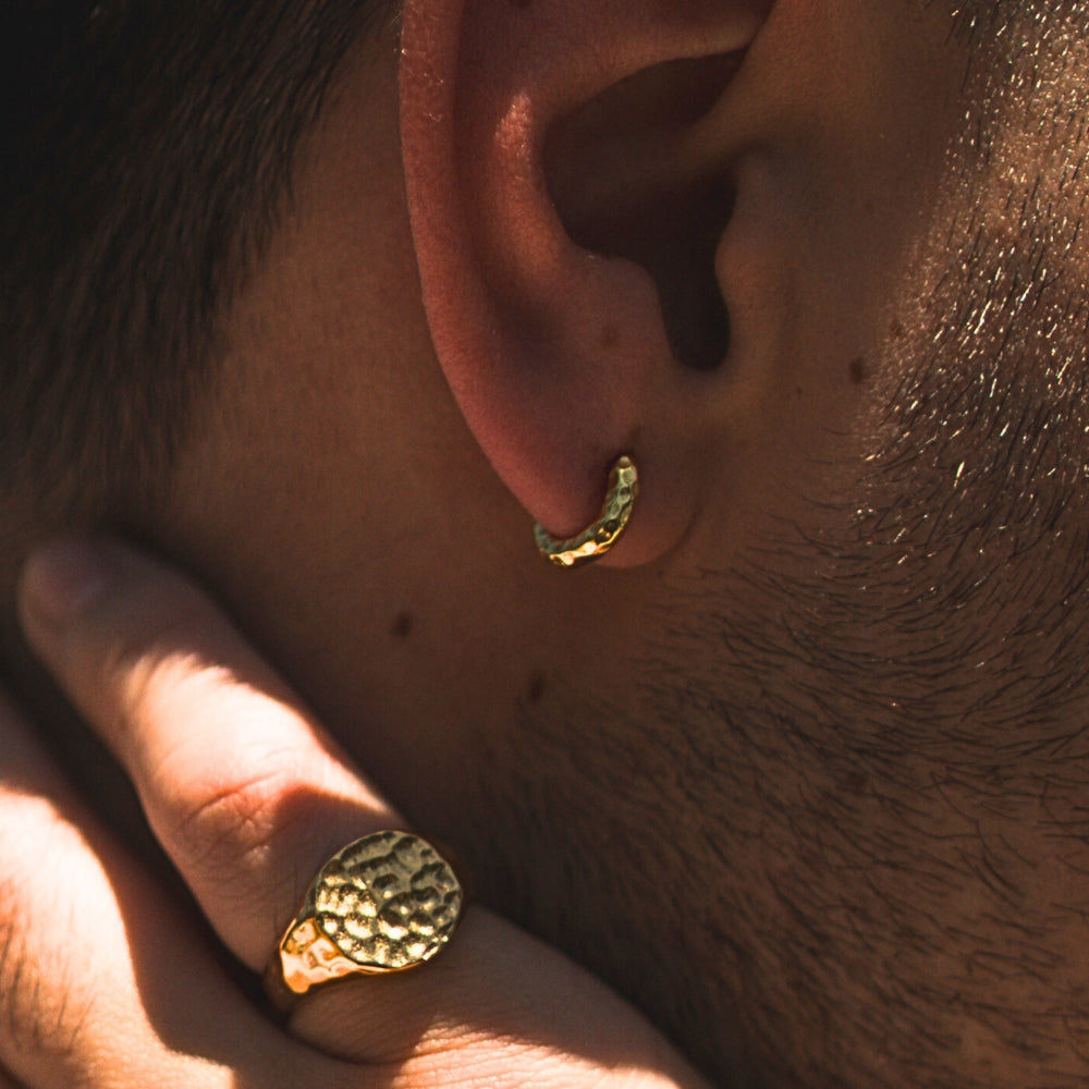 Close-up of a person wearing gold hoop earrings and a ring.