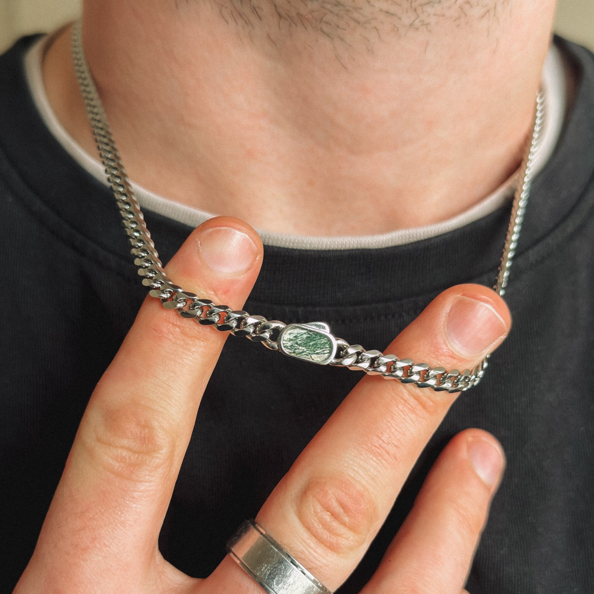 Close-up of a silver chain necklace with a green gemstone held by a person.