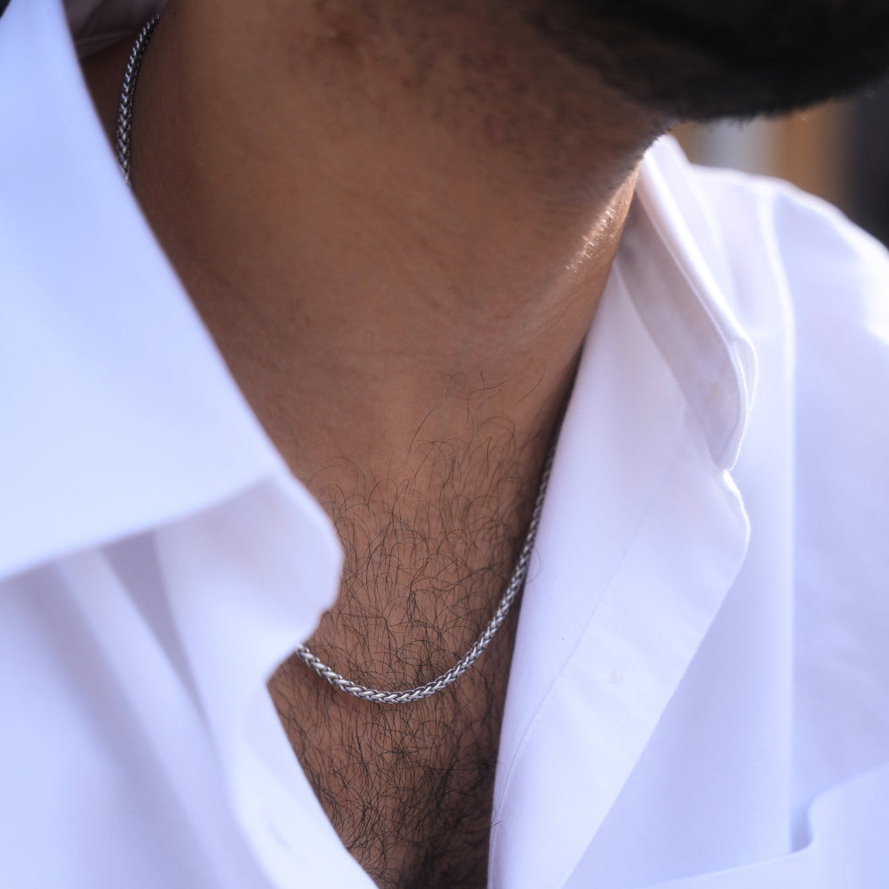 Close-up of a person wearing a silver chain necklace with a blurred background
