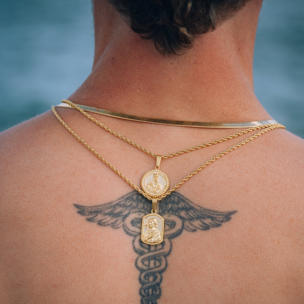 Person wearing gold necklaces with pendants against a blurred natural background