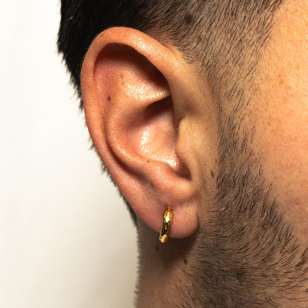 Close-up of an ear wearing a gold hoop earring with a plain background