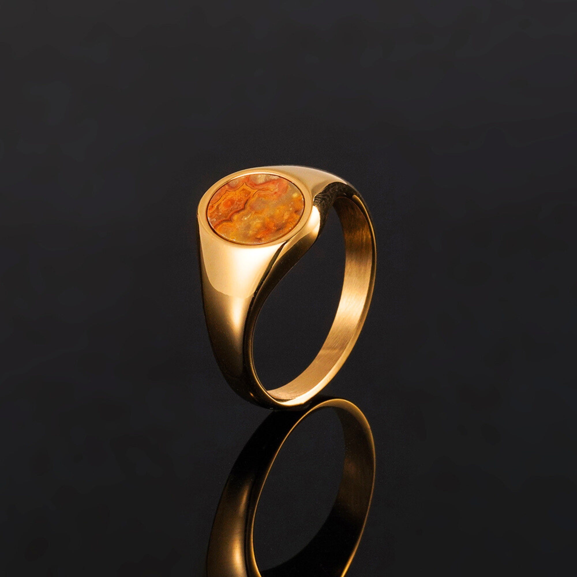 Gold ring with a round orange stone on a black background