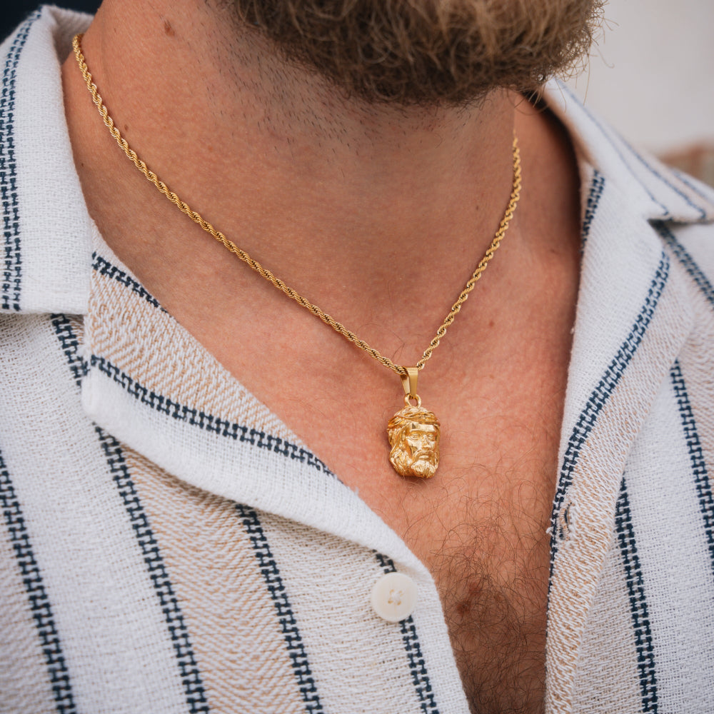 Gold necklace with a pendant worn by a person in a white shirt with blue stripes.