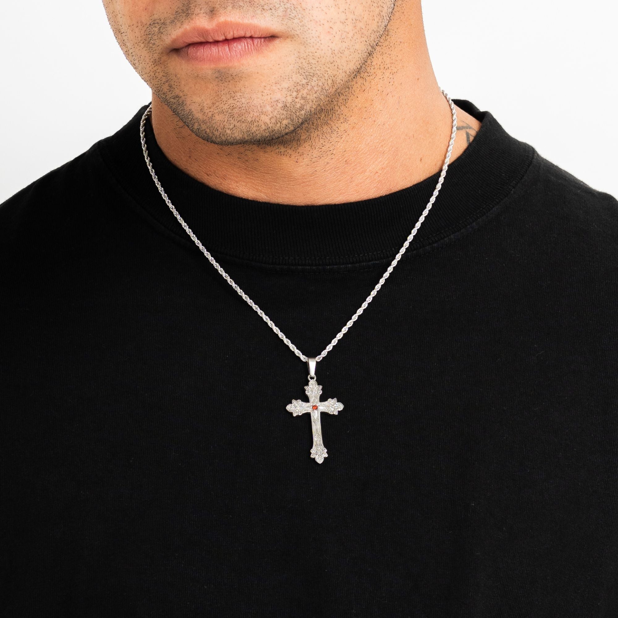 A silver cross pendant necklace with a small red cross accent in the center, worn by a man in a black crewneck shirt against a white background.