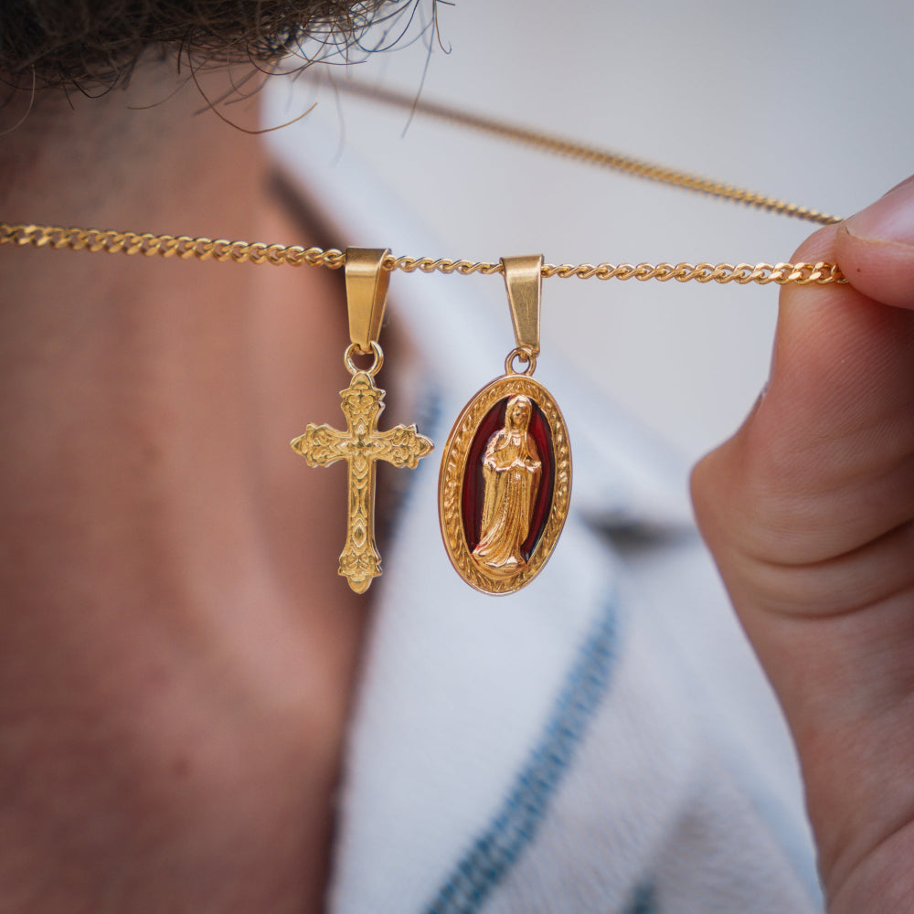 Gold necklace with a cross and religious pendant held by a person.