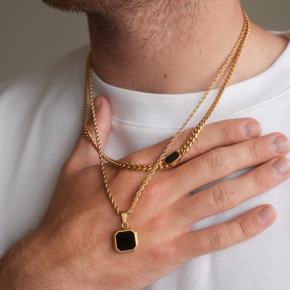 Gold chain with a black pendant worn by a person on a plain background