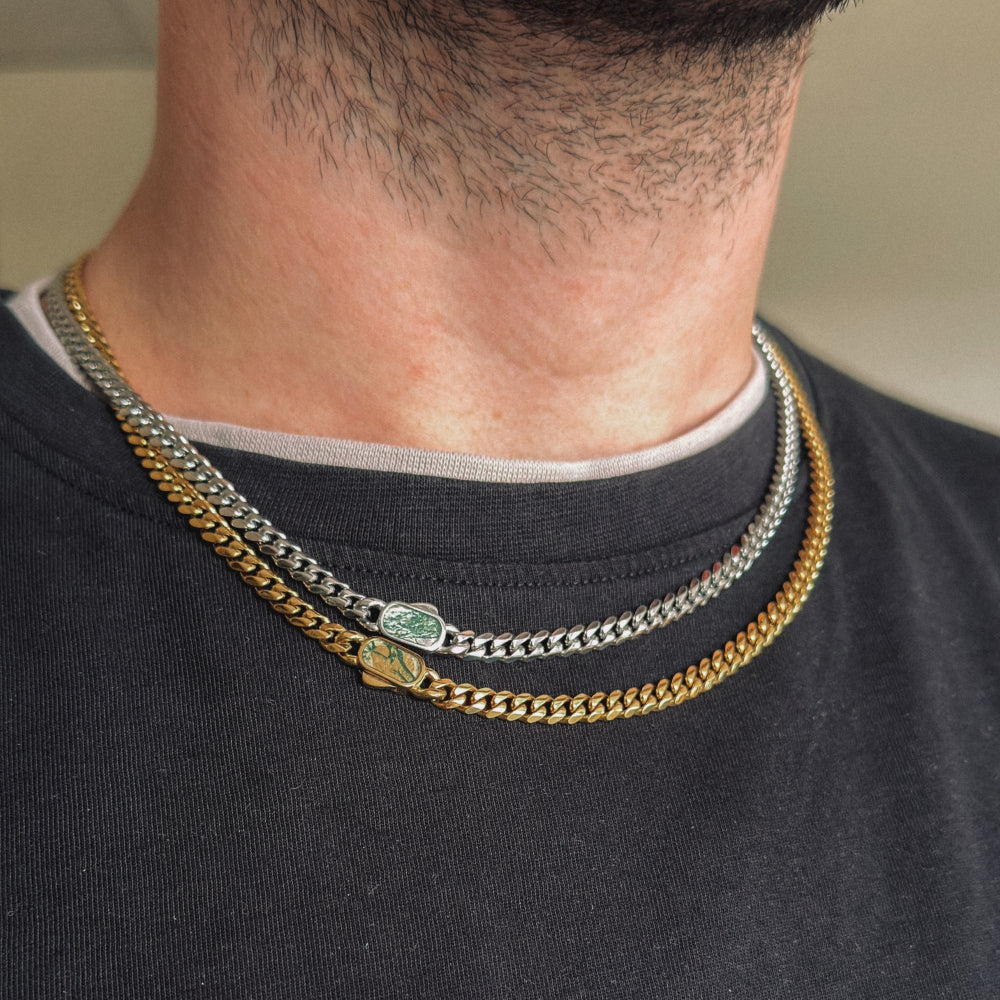 Close-up of a person wearing two chain necklaces on a plain background