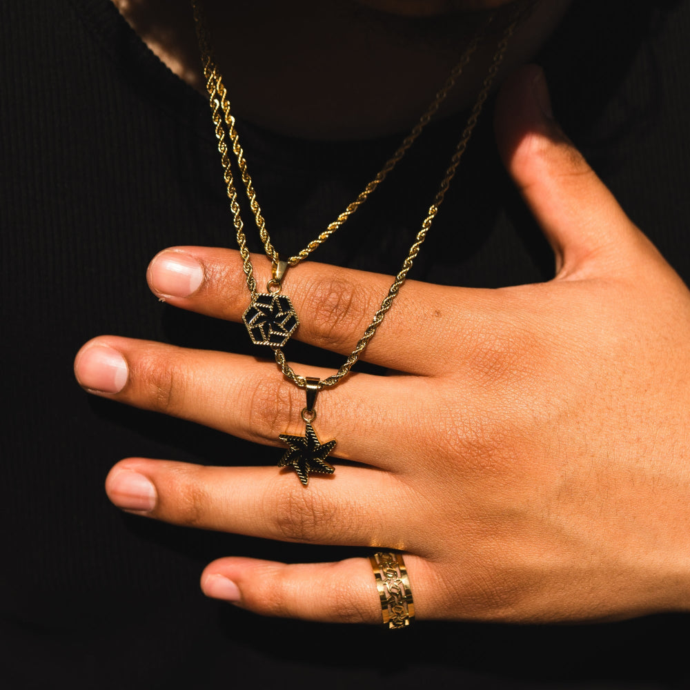 Hand wearing a gold necklace and ring on a black background