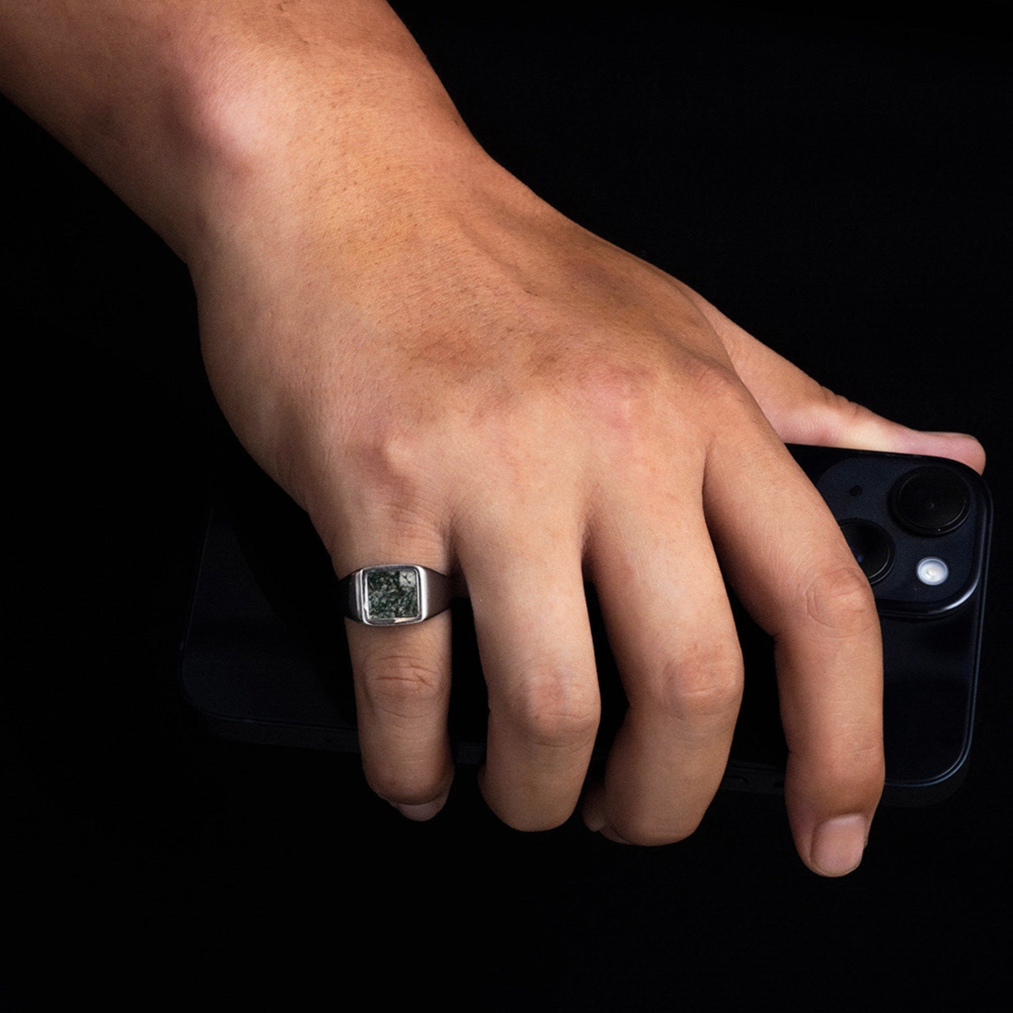 Hand wearing a ring holding a smartphone on a black background