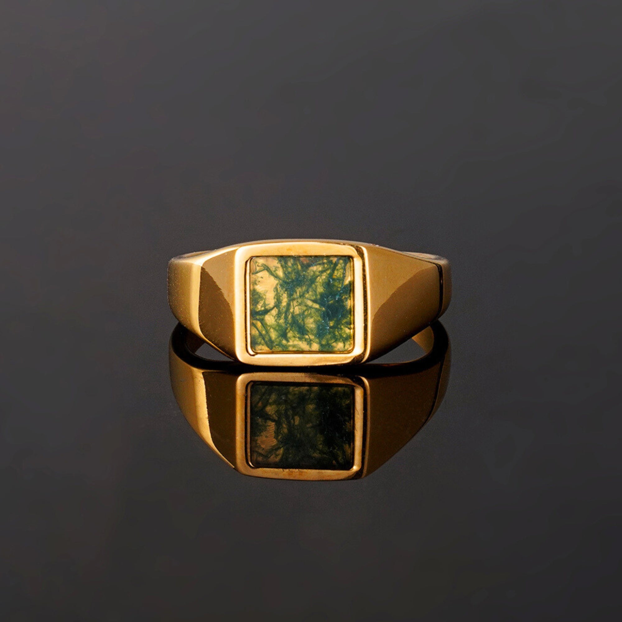 Gold ring with a green stone on a reflective black surface