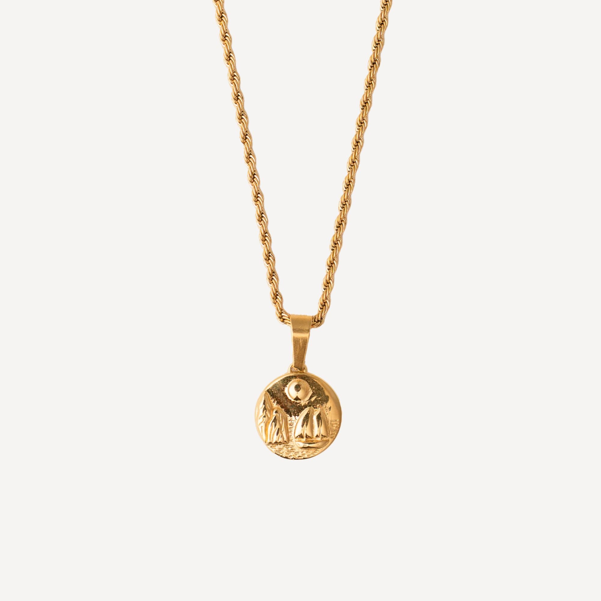 A gold chain necklace with a circular pendant featuring an engraved figure, shown against a solid off-white background.