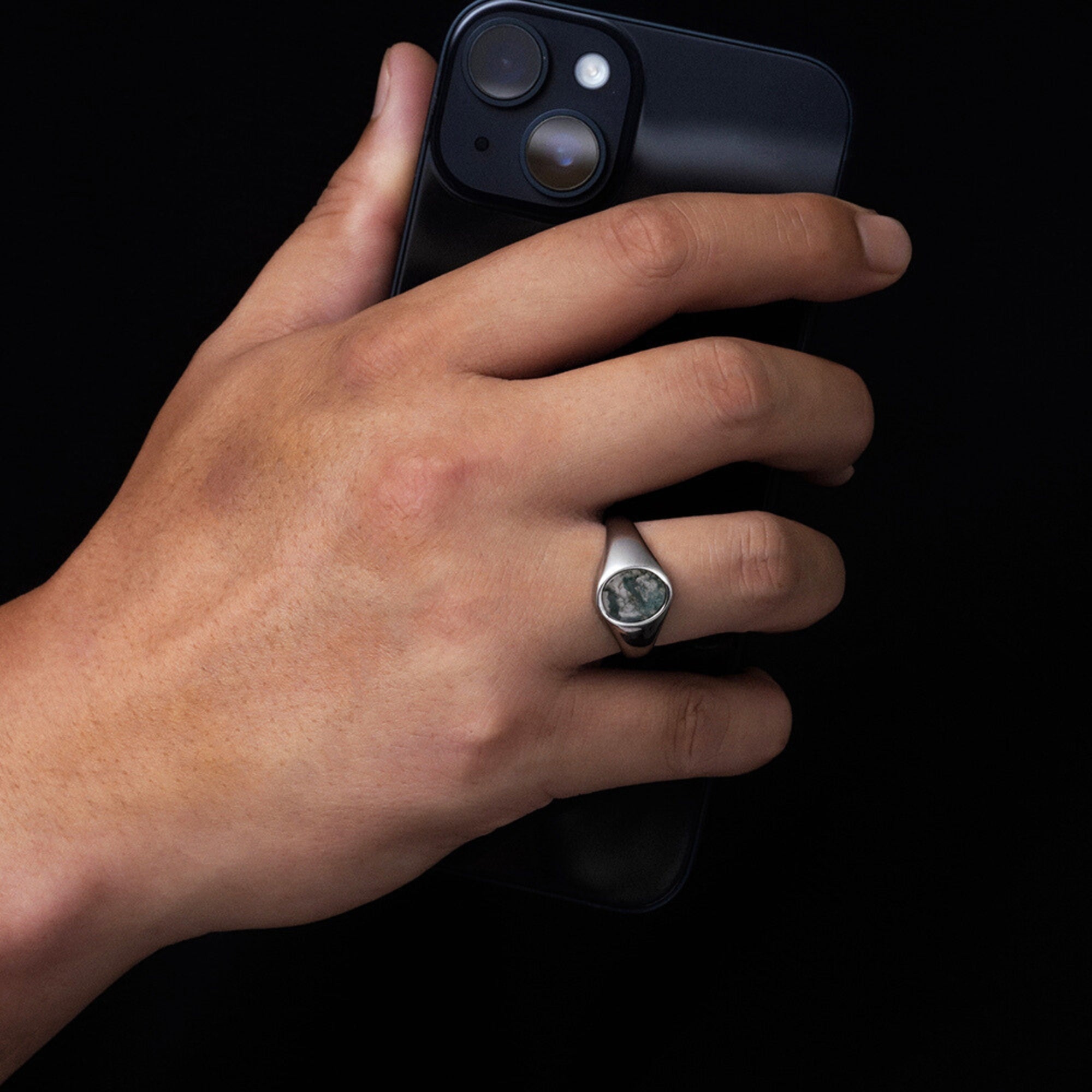 Hand holding a smartphone with a ring on a black background