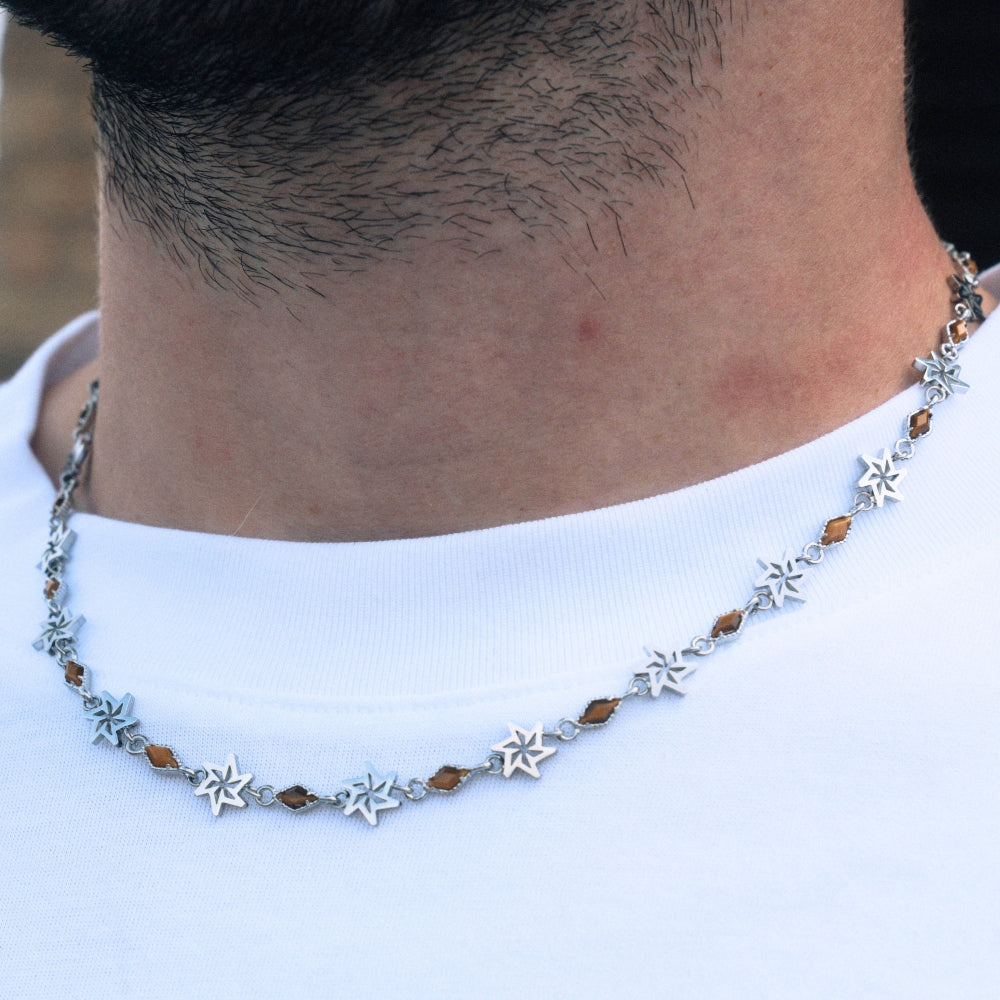 Close-up of a necklace with star and brown bead design on a white shirt.