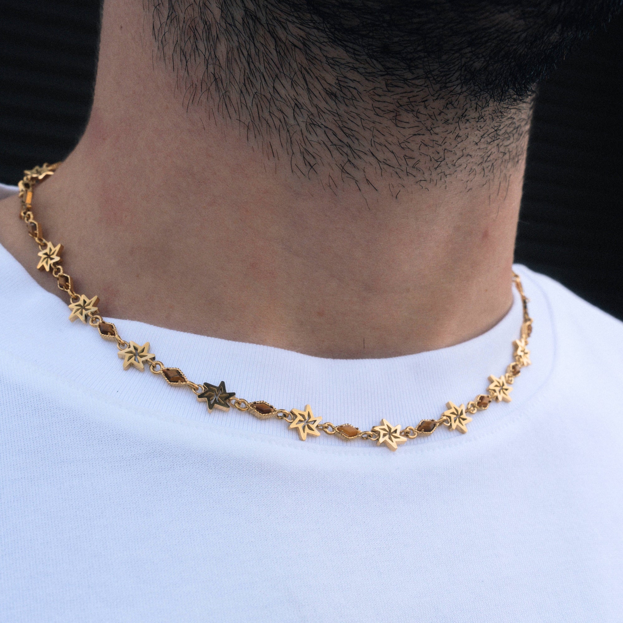 Gold star necklace worn by a person on a plain background