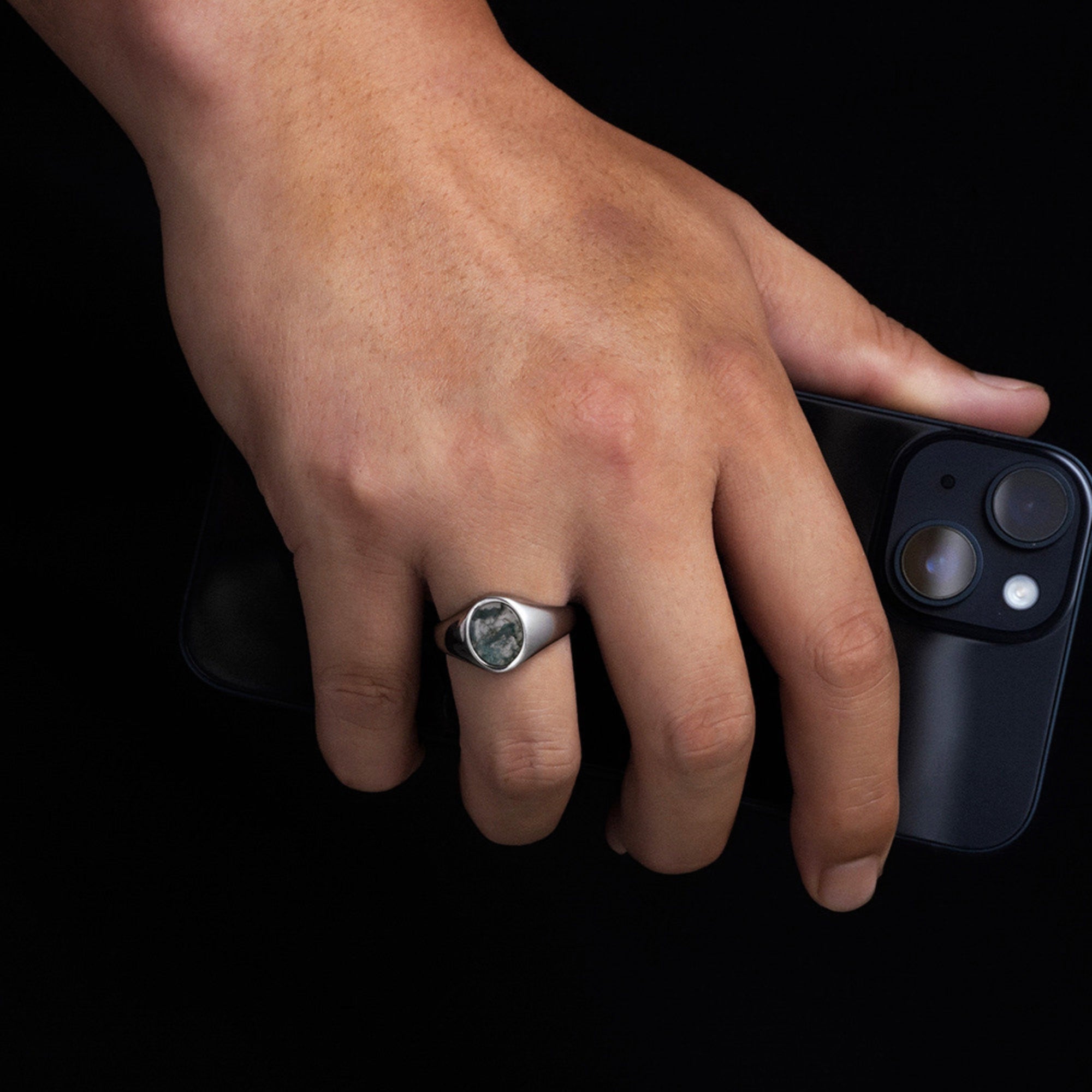 Hand wearing a ring holding a smartphone on a black background