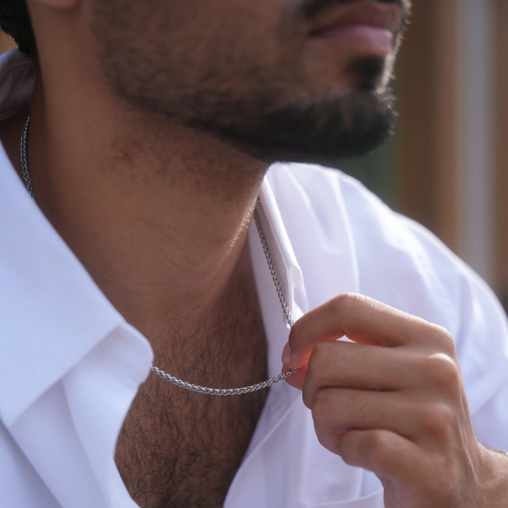 Man adjusting a silver chain necklace with a blurred background