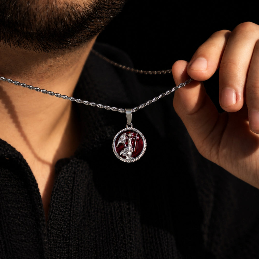 Person holding a silver necklace with a detailed pendant against a dark background