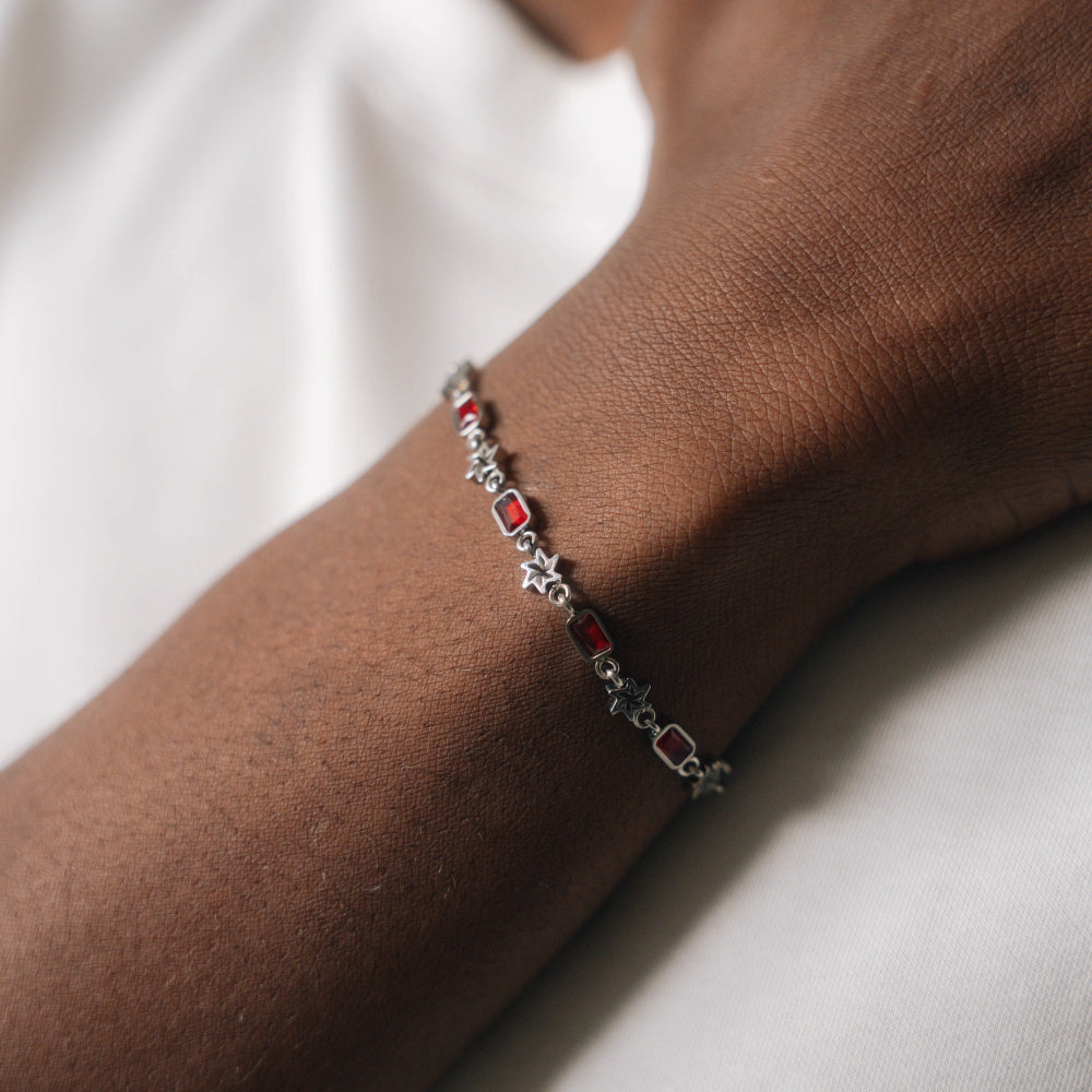 Bracelet with red stones on a wrist against a neutral background