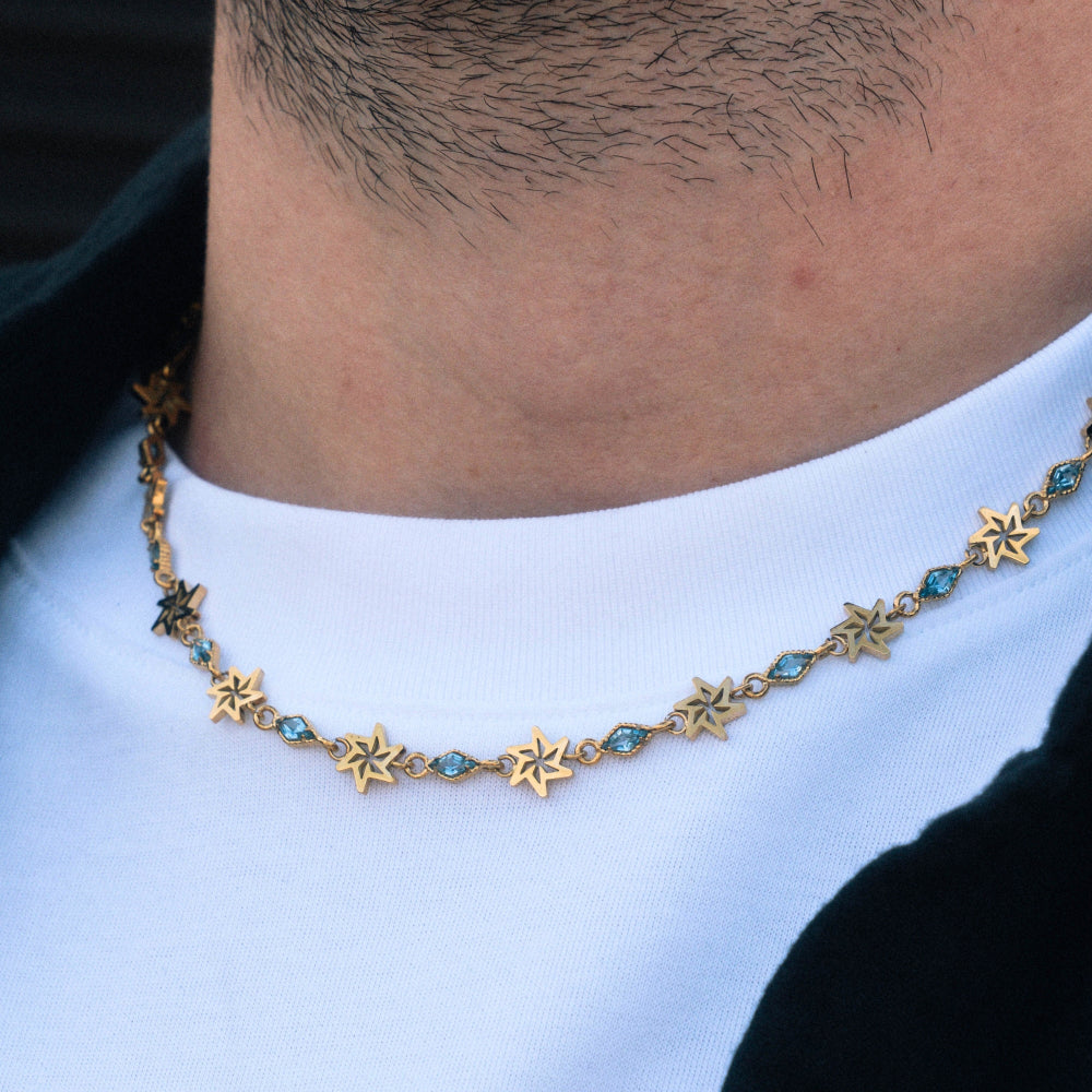 Necklace with star and blue stone design worn by a person against a white shirt background