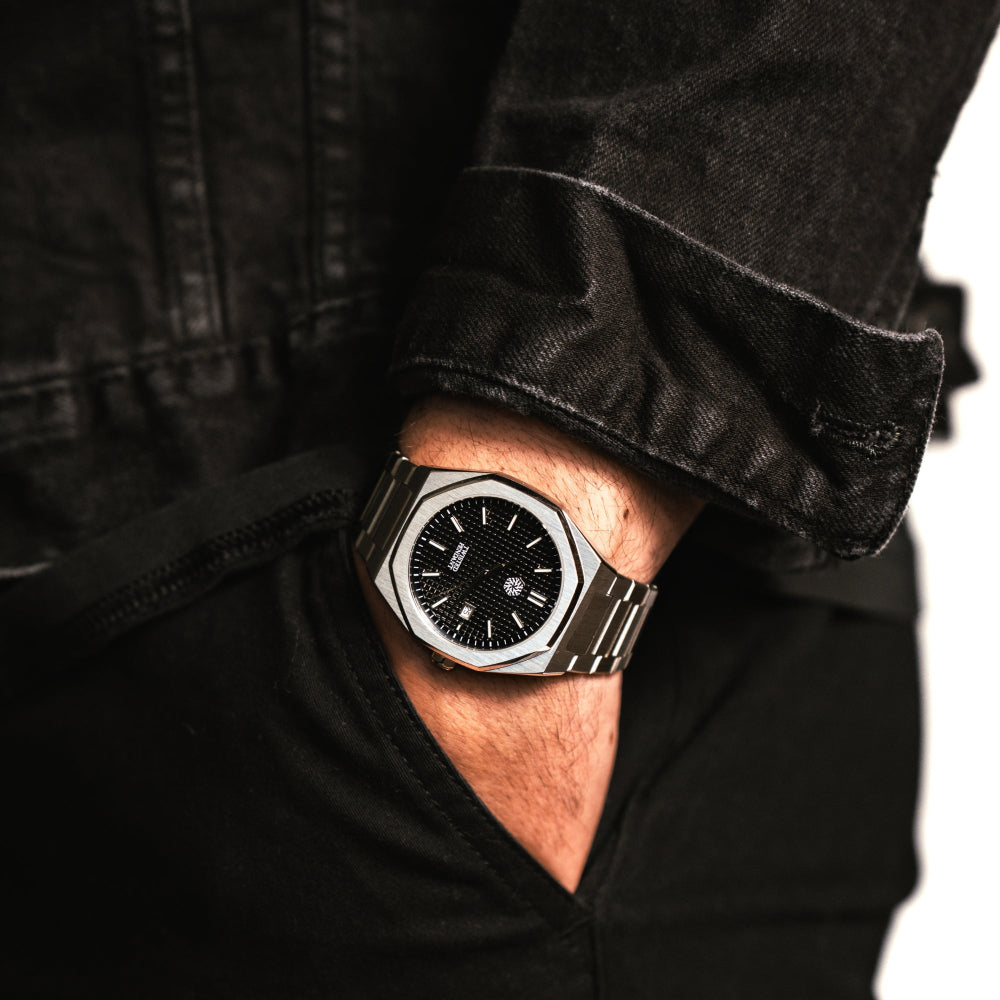 Person wearing a black and silver watch with a dark jacket.