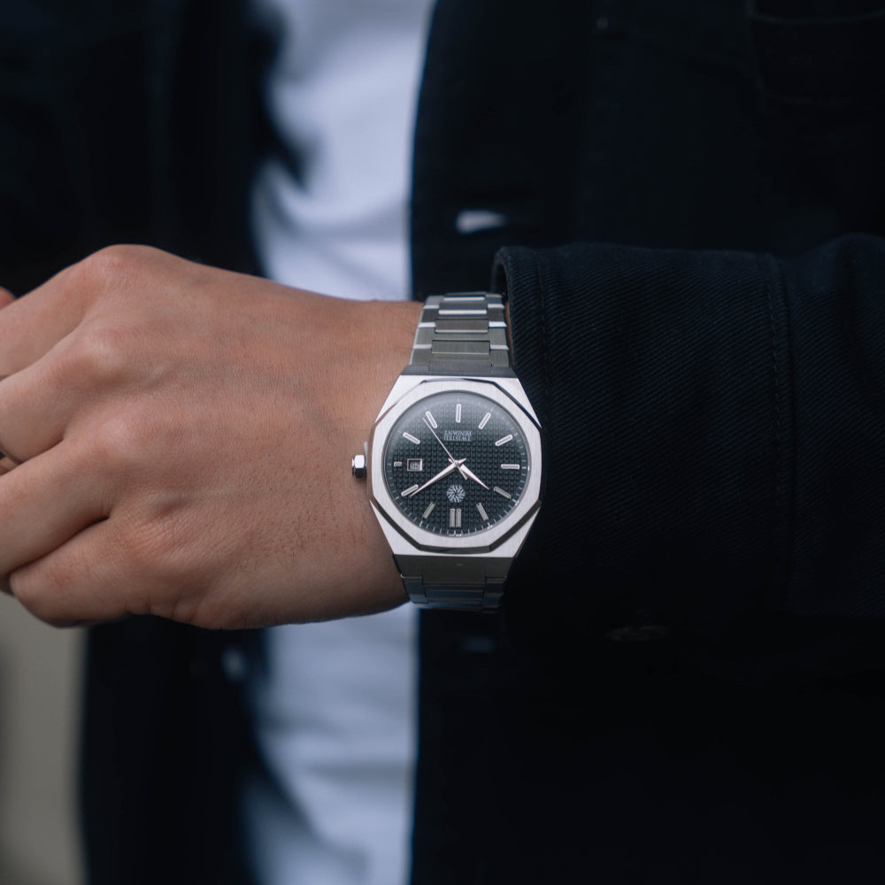 Person wearing a silver watch with a dark face on a blurred background