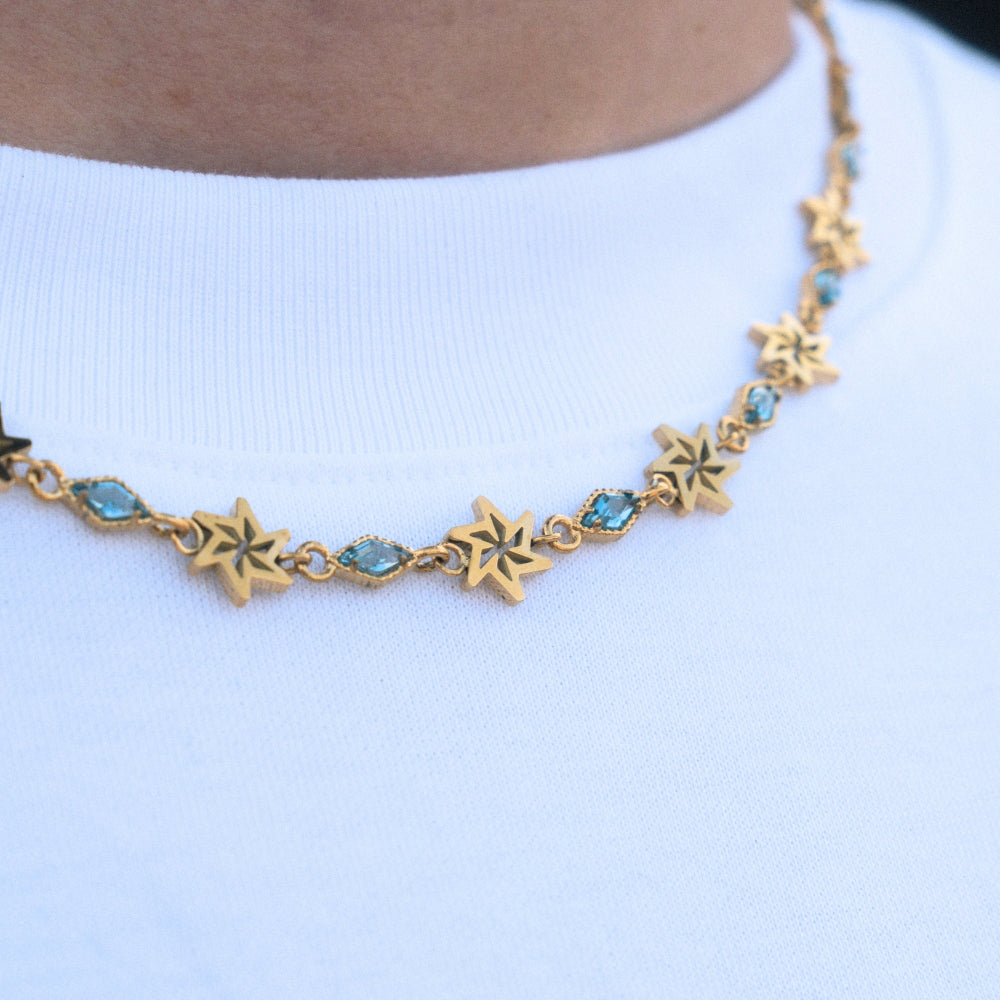 Gold necklace with star-shaped pendants and blue stones on a white background