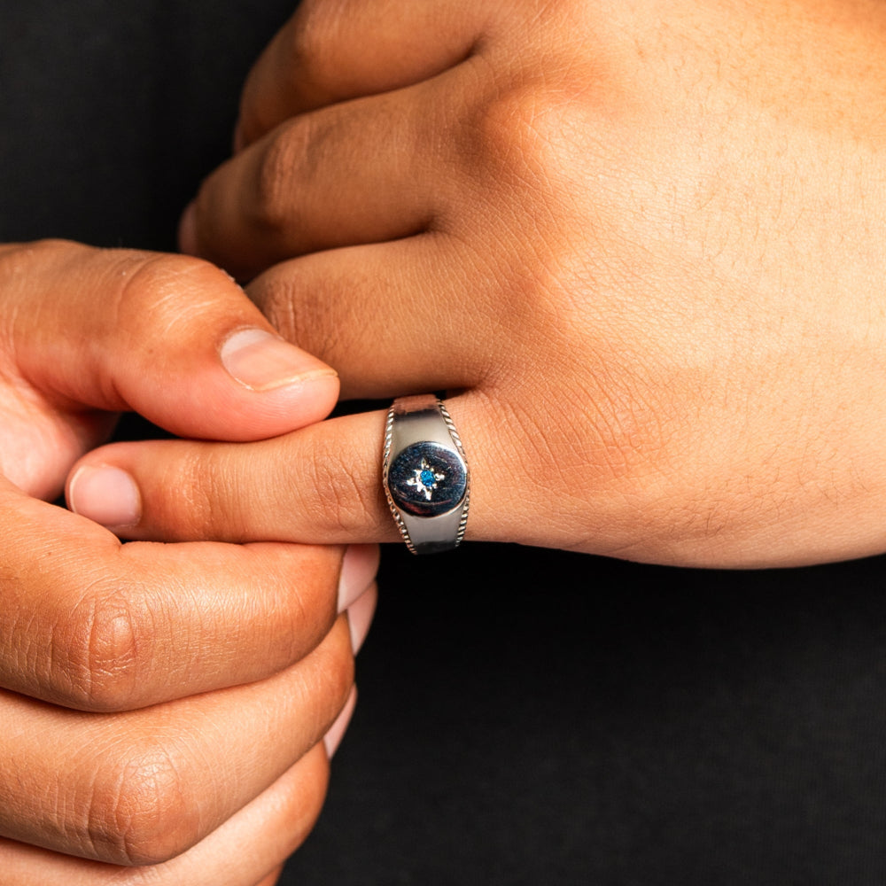 Close-up of a hand wearing a silver ring with a blue gemstone on a dark background