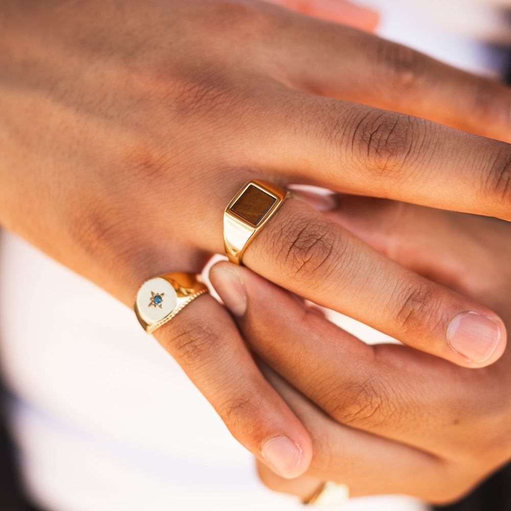 Close-up of a hand wearing two gold rings with a blurred background