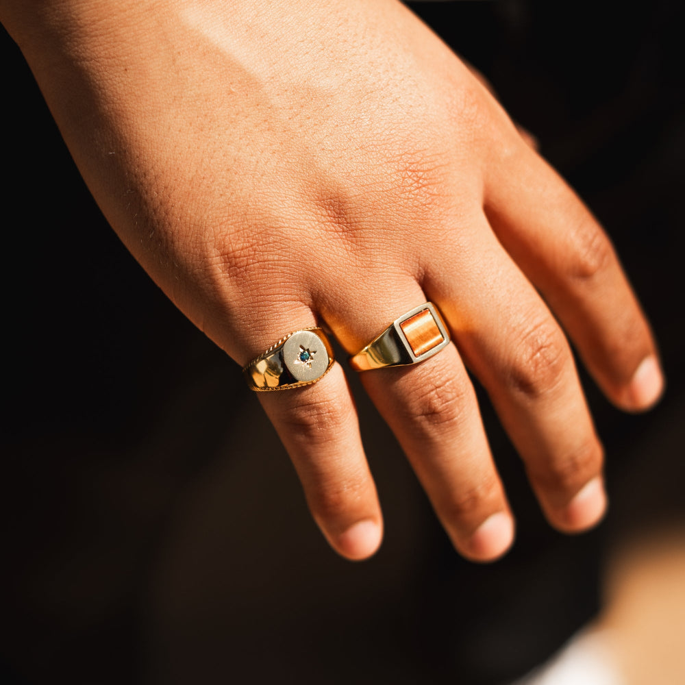 Hand wearing two gold rings with a dark background