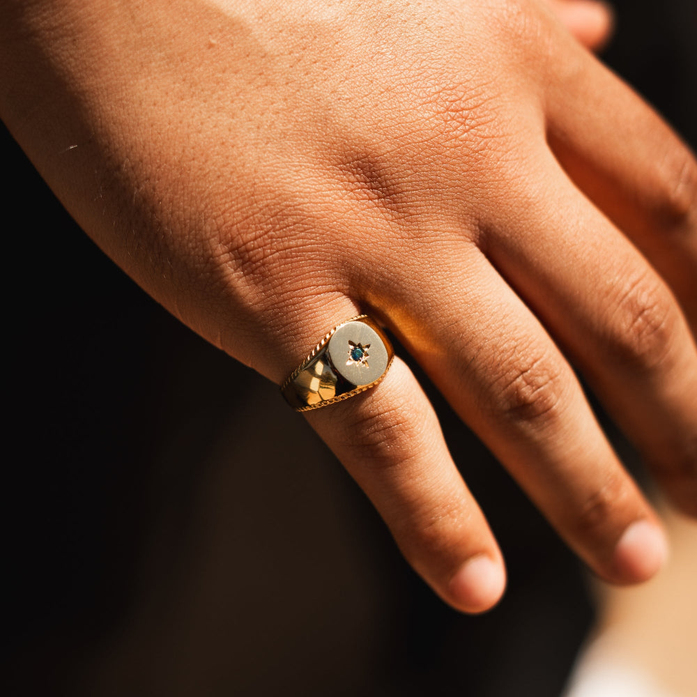 Close-up of a hand wearing a gold ring with a dark gemstone on a dark background