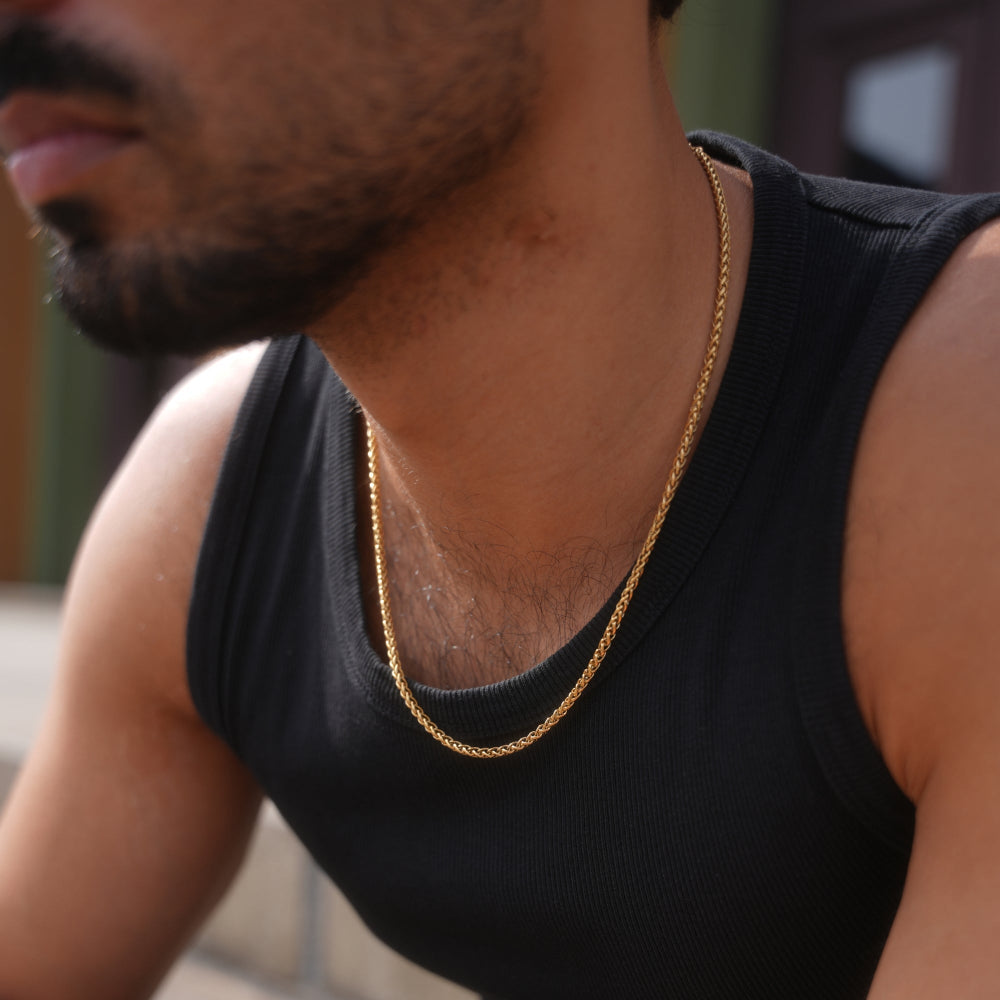 Man wearing a black tank top and gold chain, with a blurred background